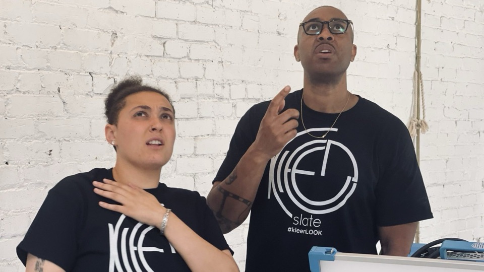 Two KleenSlate crew members in tees on a white-brick set
